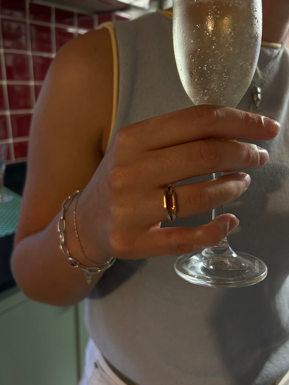 A close-up lifestyle shot of a person holding a sparkling champagne flute, wearing a gold ring with a geometric design on their ring finger.