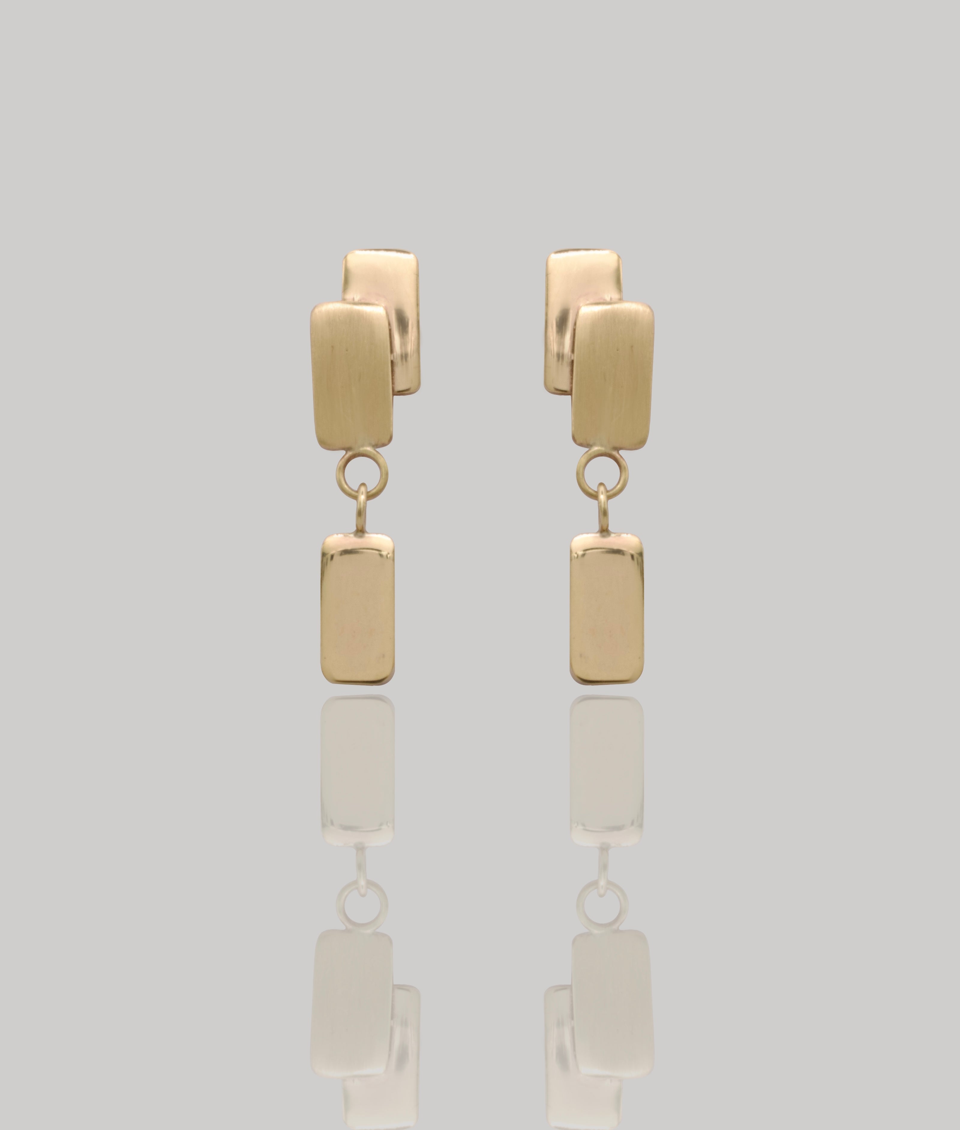 Gold earrings with rectangular pendants on a light gray background