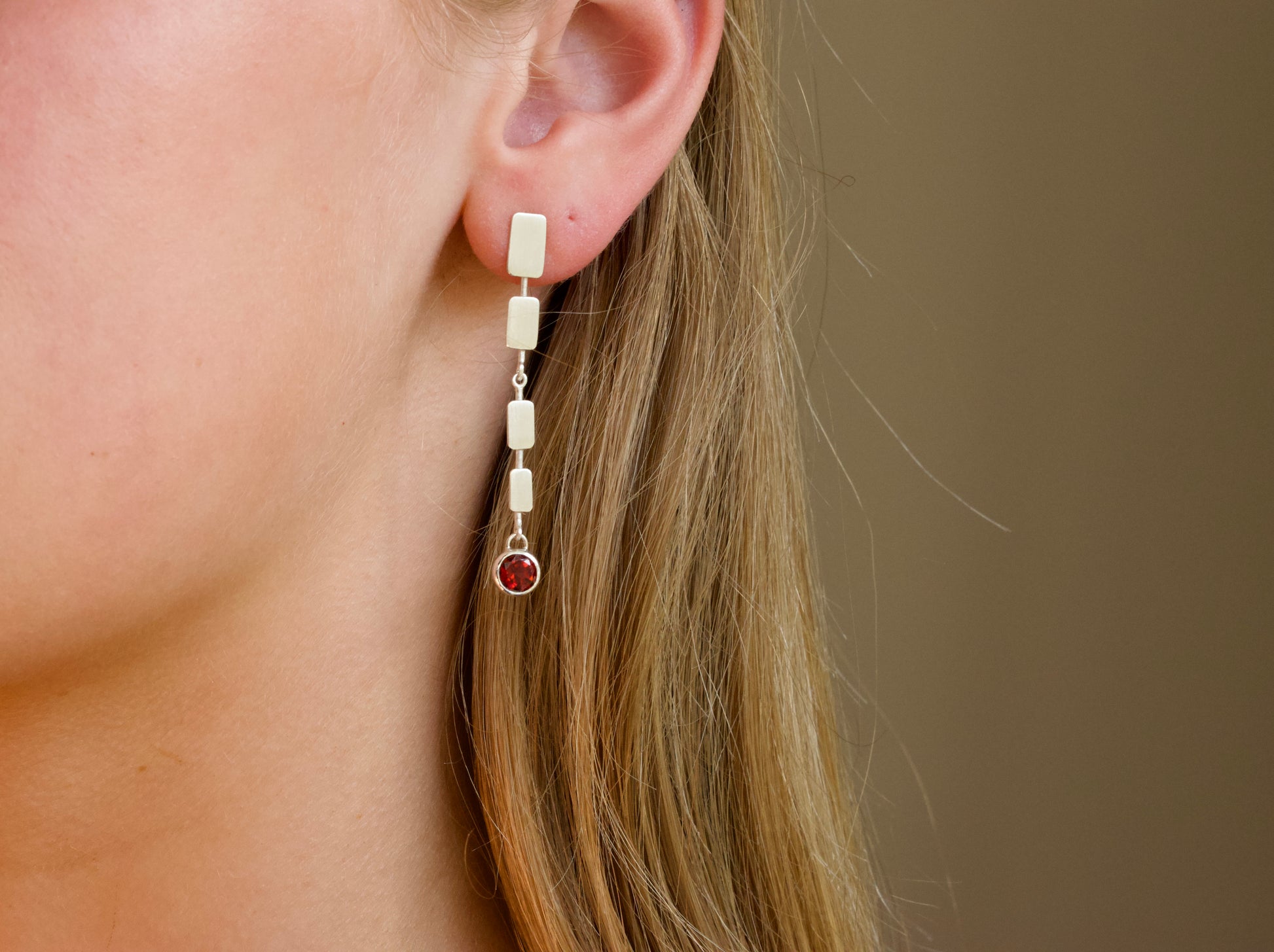 Long silver earrings with red gemstone on blonde person.