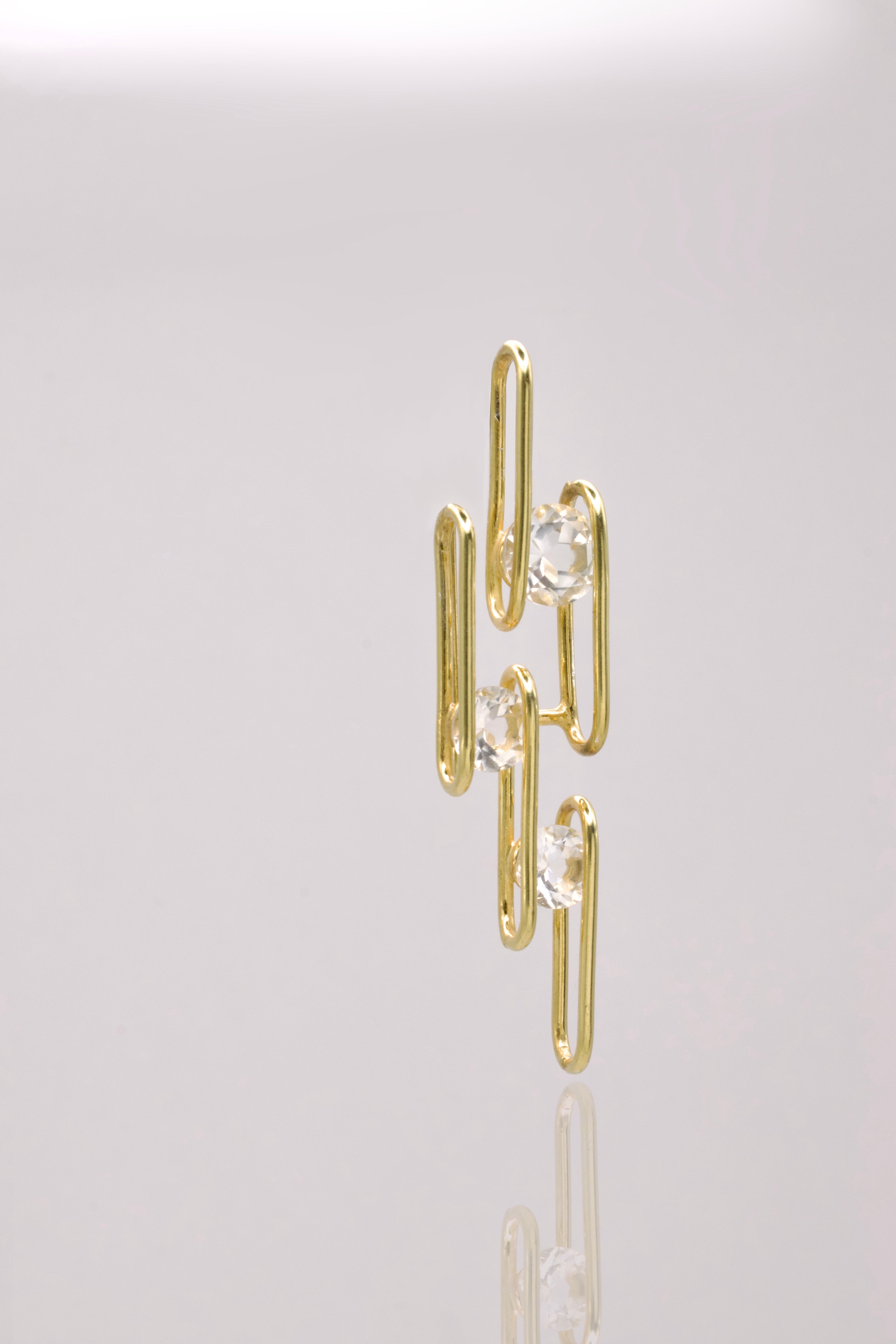 Gold wire earring with clear gemstones on a light gray background
