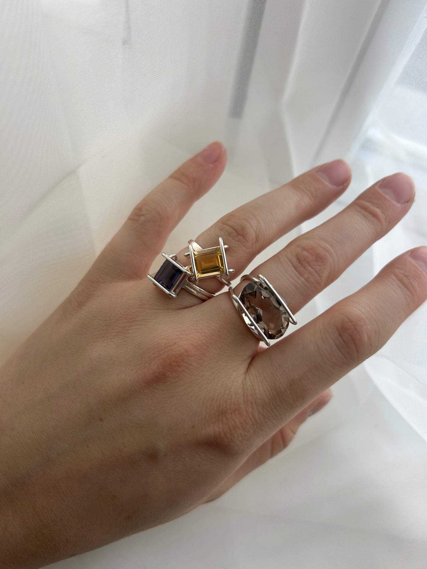 Hand wearing multiple rings with gemstones on a white background