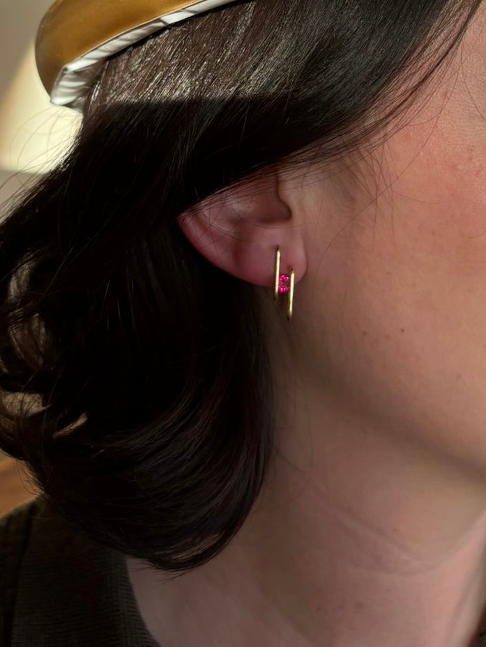 Close-up of an ear wearing a gold earring with a pink gemstone.