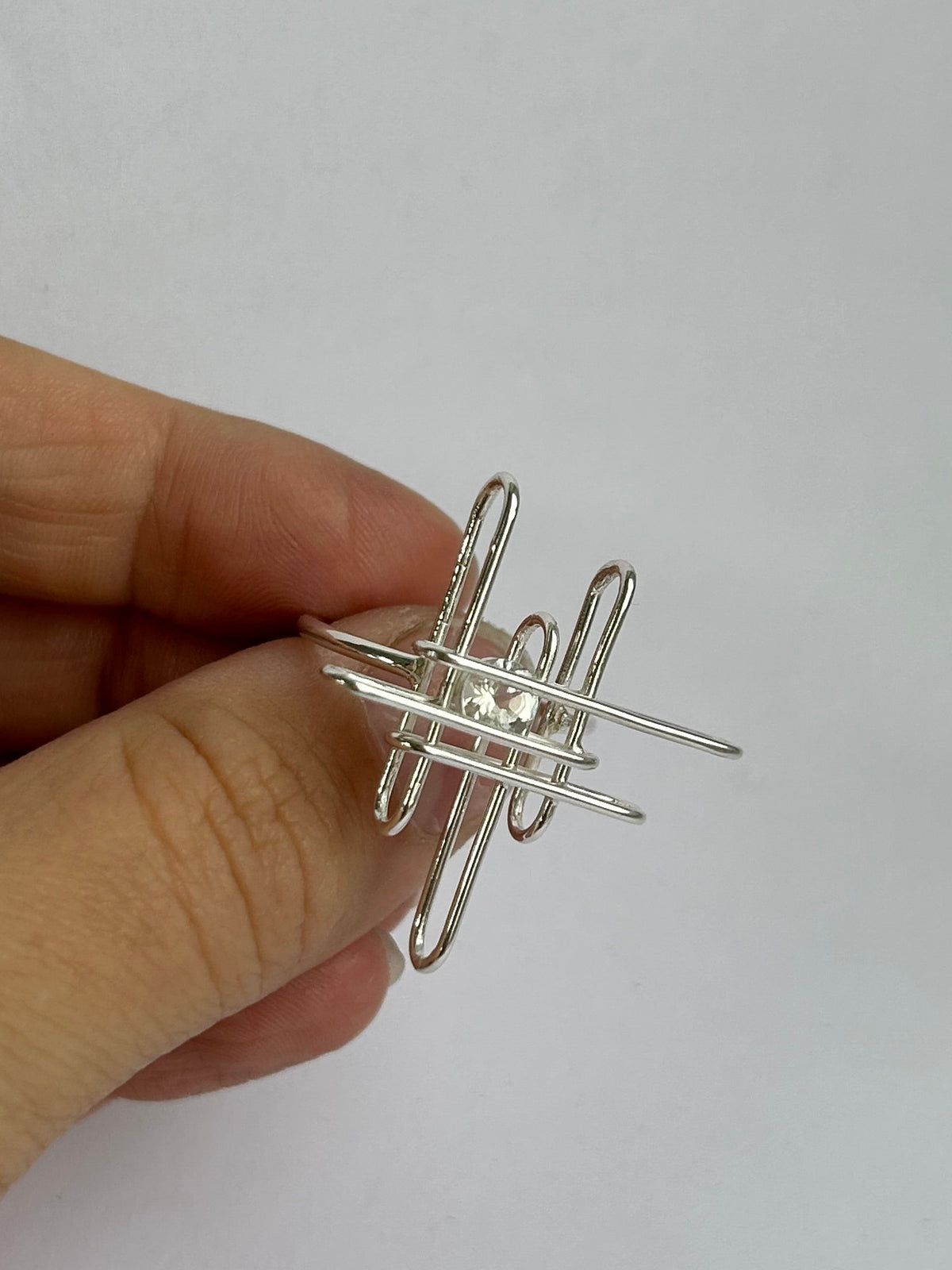 Hand holding a silver wire ring against a white background