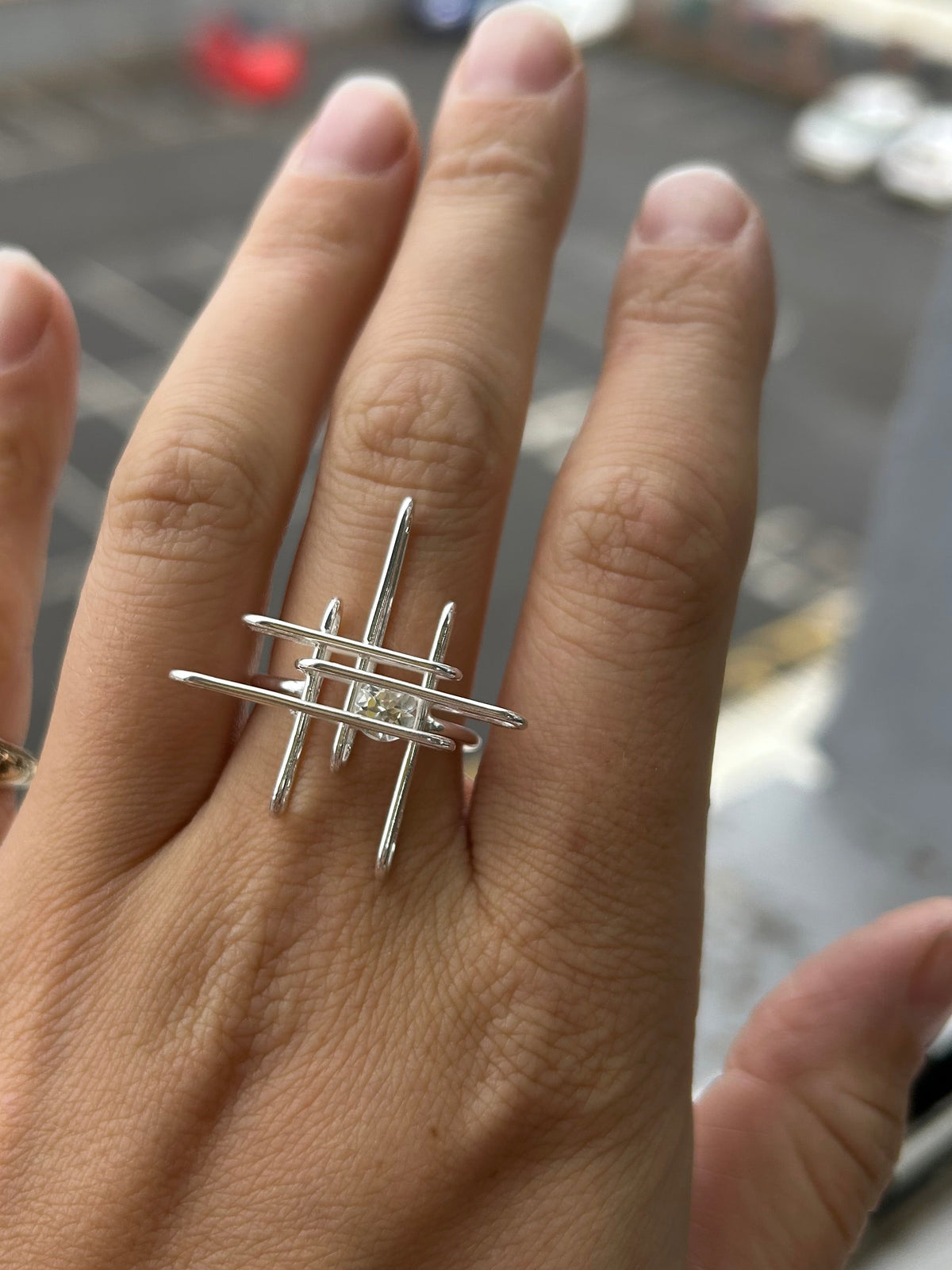 Hand wearing a silver ring with a blurred city street background