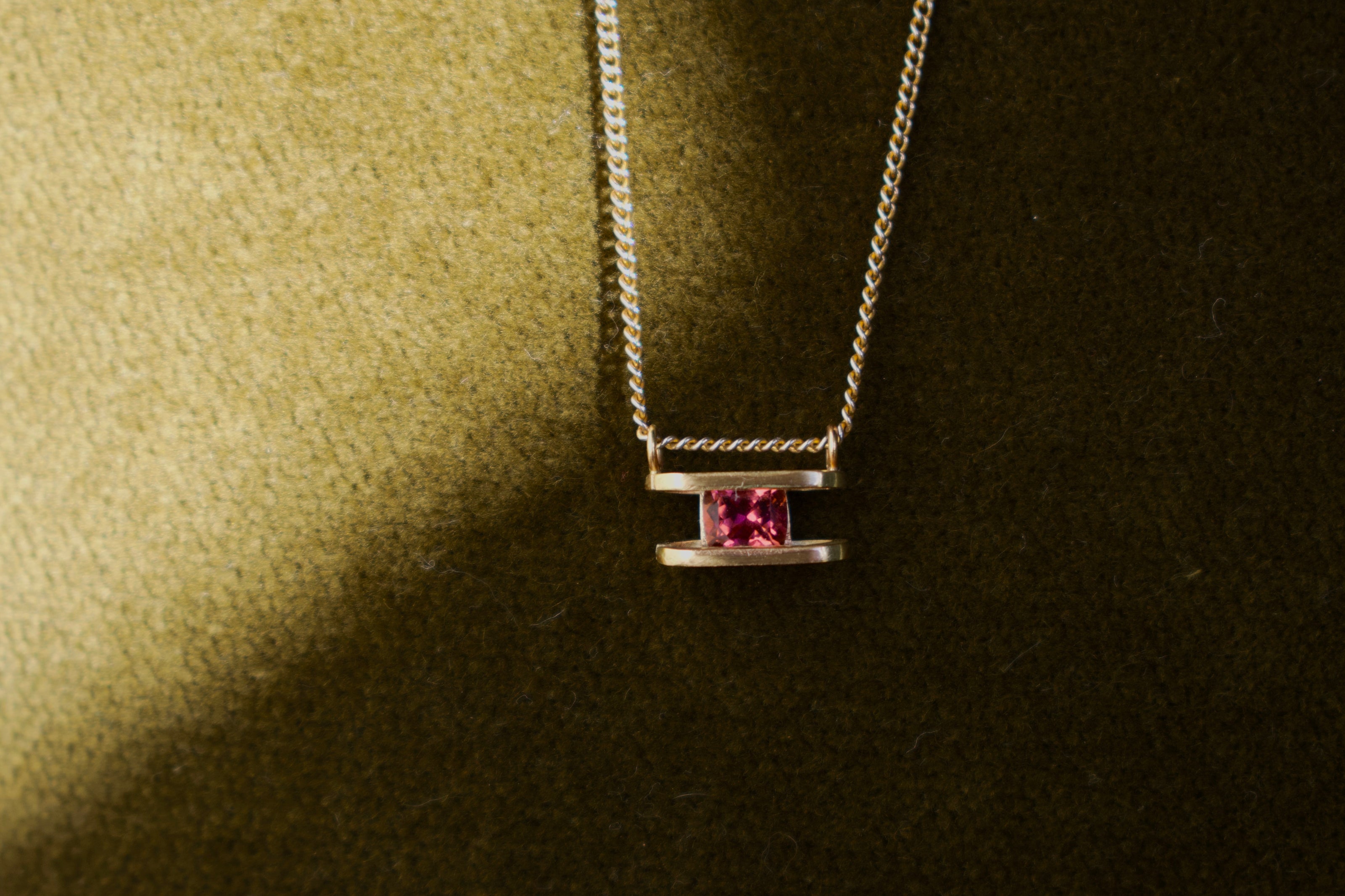 Necklace with a pink gemstone pendant on a green textured surface